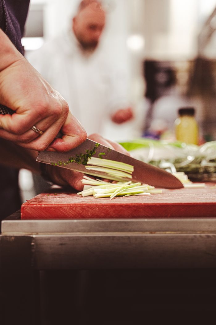 About Close-up of a chef slicing vegetables in a professional kitchen setting.